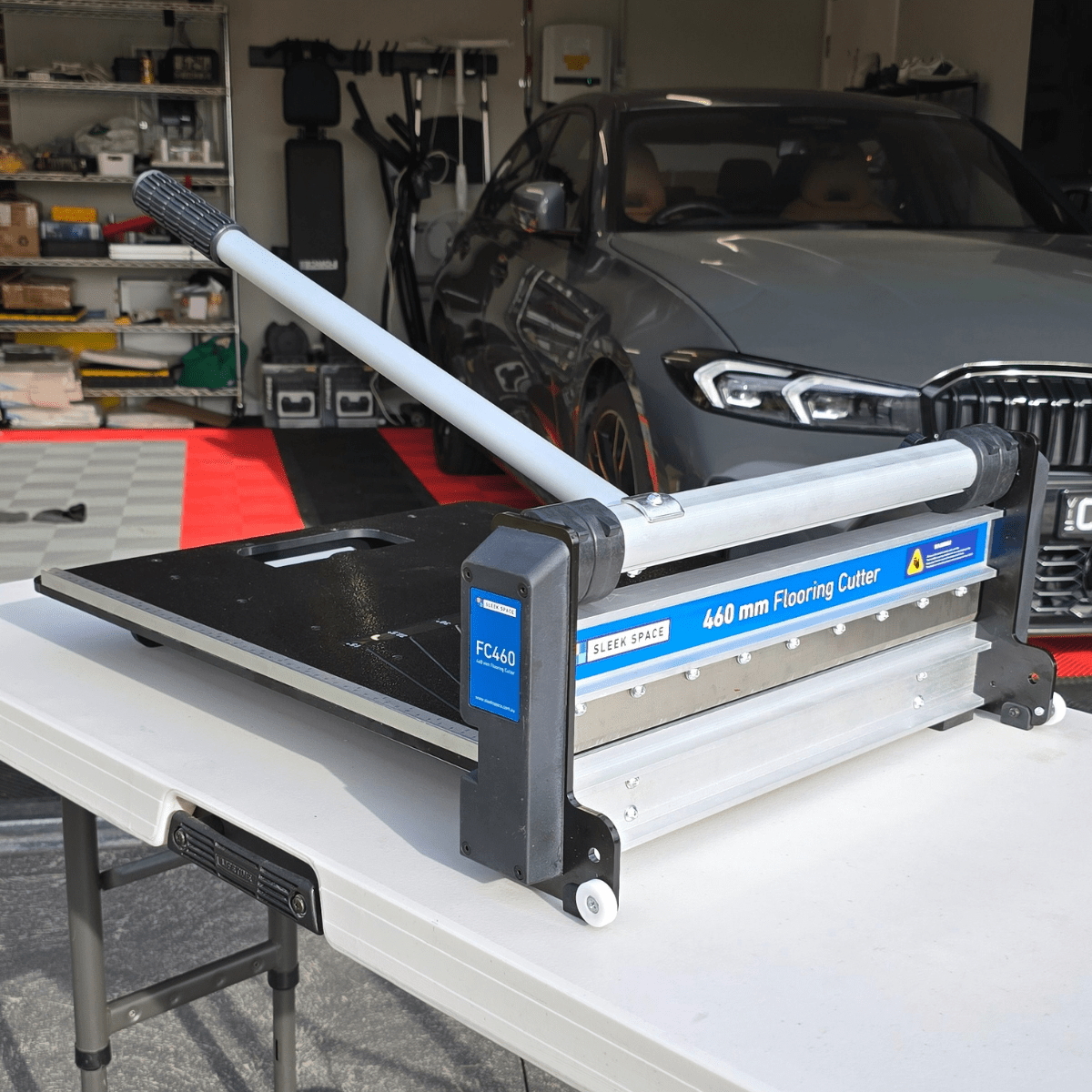 The tile cutter set up on a bench in a garage, a car parked behind