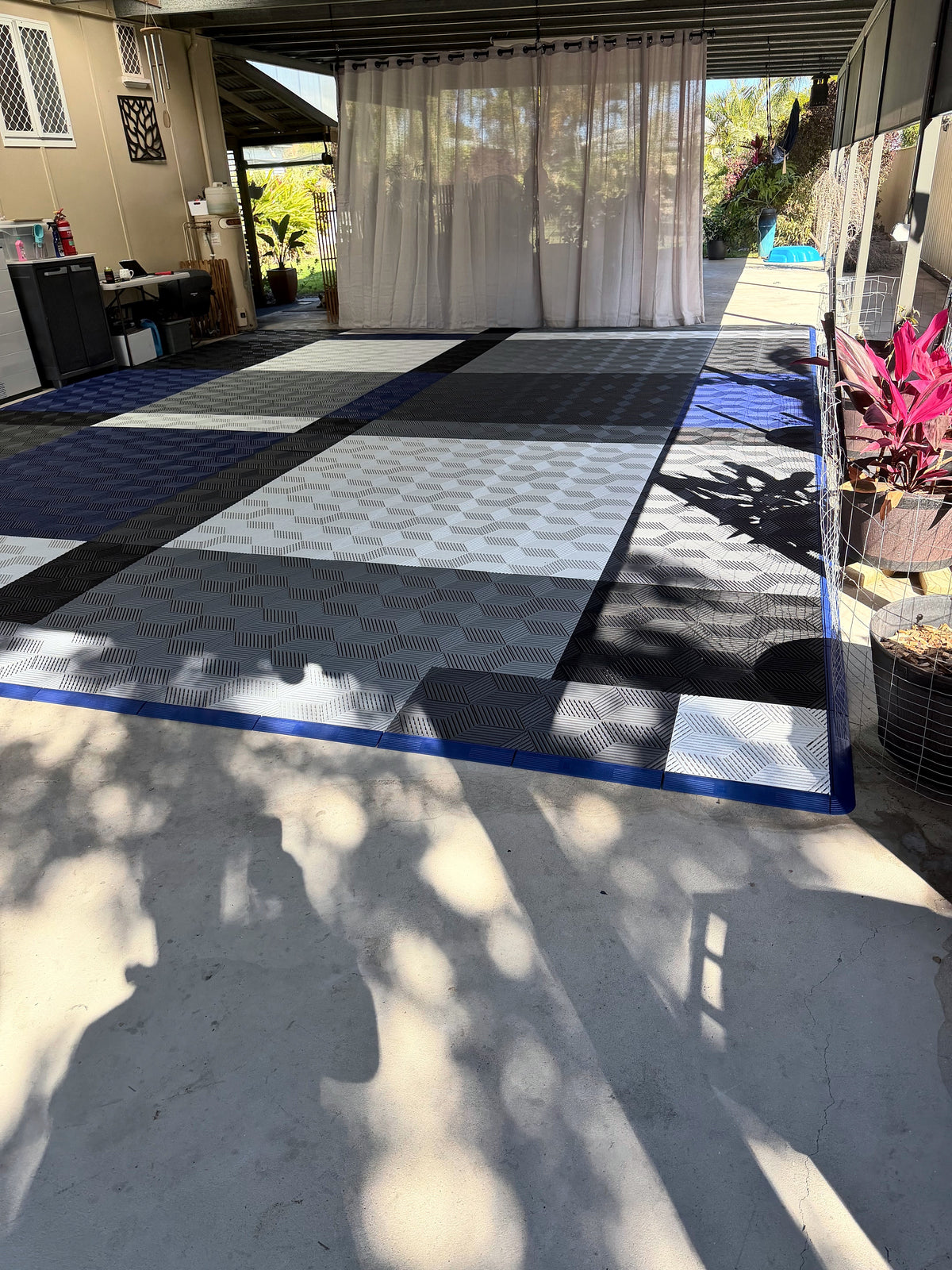 A customer's carport floor in ULTRACUBE tiles, five colours edged with Night Blue ULTRAEDGE ramps, seen from the driveway
