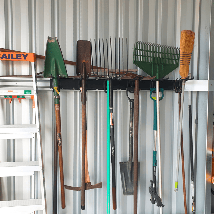 Two ULTRARACK rails on a corrugated shed wall holding a rake, a pitchfork, shovels, a broom and loppers above a clear floor