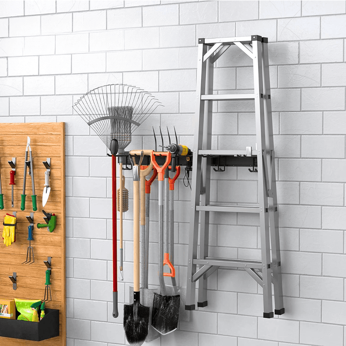 An ULTRARACK rail on a white brick garage wall holding a rake, garden fork and shovels beside a ladder