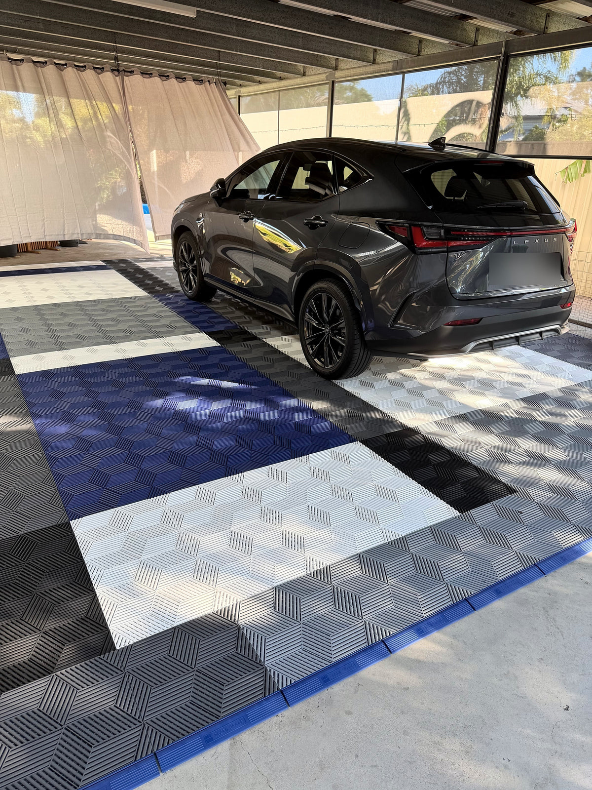 A customer's carport floor in ULTRACUBE tiles, five colours edged with Night Blue ULTRAEDGE ramps, a car parked on it